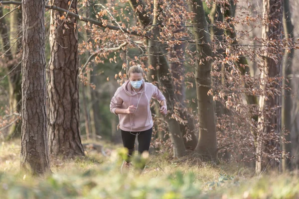 El virus Corona, o Covid-19, se está extendiendo por todo el mundo. Retrato de mujer atlética caucásica con una máscara facial de protección médica mientras corre en la naturaleza . —  Fotos de Stock