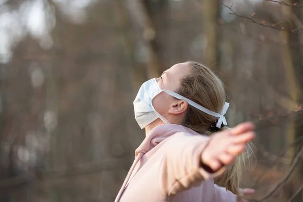 Portrait of caucasian sporty woman wearing medical protection face mask while relaxing by taking a deep breath in forest. Corona virus, or Covid-19, is spreading all over the world — Stock Photo, Image