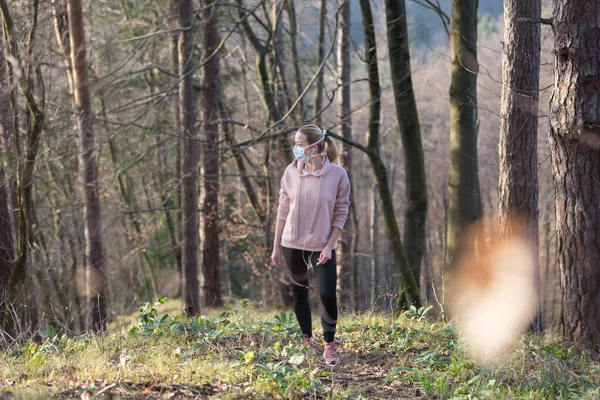 Corona virus, of Covid-19, verspreidt zich over de hele wereld. Portret van een blanke sportieve vrouw met een medisch beschermend gezichtsmasker tijdens het wandelen in het bos. Coronavirus. — Stockfoto