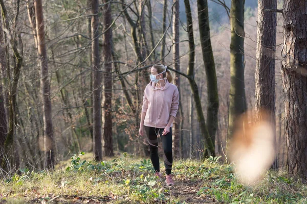 Das Coronavirus oder Covid-19 breitet sich auf der ganzen Welt aus. Porträt einer kaukasischen sportlichen Frau, die beim Spazierengehen im Wald eine medizinische Schutzmaske trägt. Coronavirus. — Stockfoto