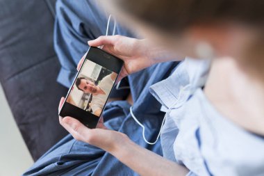Kanepede uzanan bir kadın Corona virüsü salgını sırasında sevdikleriyle görüntülü konuşma yapmak için telefonla sosyal medyayı kullanıyor. Evde kal, sosyal mesafeli yaşam tarzı.