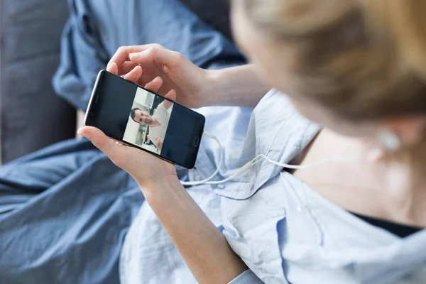 Mujer en casa relajándose en el sofá utilizando las redes sociales en el teléfono para el chat de vídeo con sus seres queridos durante la pandemia del virus corona. Quedarse en casa, estilo de vida social distanciamiento. — Foto de Stock