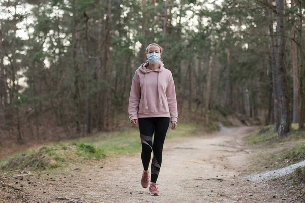 Das Coronavirus oder Covid-19 breitet sich auf der ganzen Welt aus. Porträt einer kaukasischen sportlichen Frau, die beim Spazierengehen im Wald eine medizinische Schutzmaske trägt. Coronavirus. — Stockfoto
