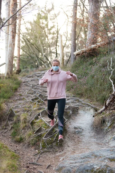 A Corona vírus, vagy Covid-19, elterjedt az egész világon. Portré fehér sportos nő visel orvosi védelem arc maszk futás közben a természetben. — Stock Fotó