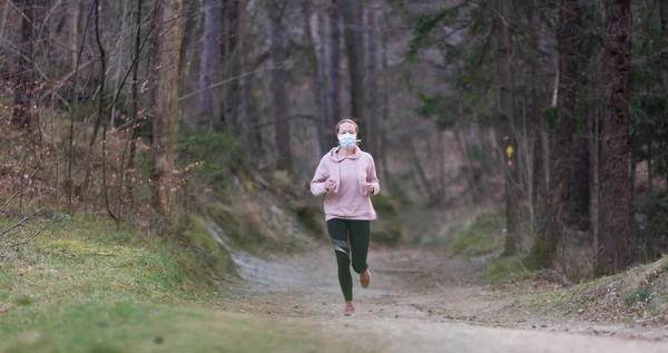 Wirus Corona, czyli Covid-19, rozprzestrzenia się po całym świecie. Portret białej sportowej kobiety noszącej maskę ochronną podczas biegania w naturze. — Zdjęcie stockowe