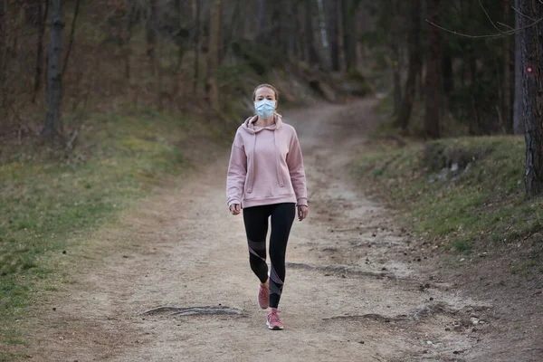 Wirus Corona, czyli Covid-19, rozprzestrzenia się po całym świecie. Portret białej sportowej kobiety noszącej maskę ochronną podczas spaceru po lesie. Wirus korony. — Zdjęcie stockowe