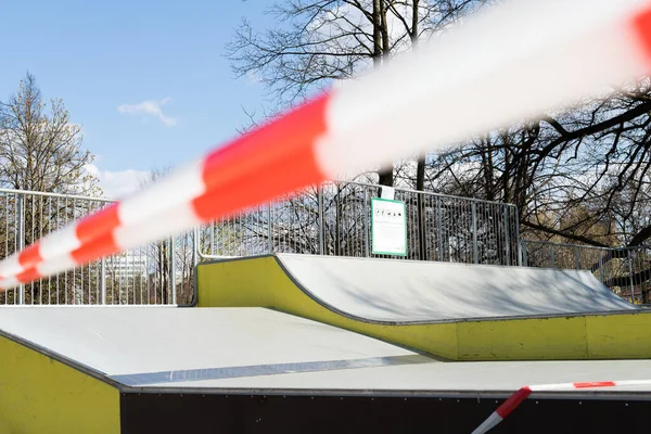 Restrição do vírus Corona COVID-19. Não há pessoas devido à quarentena. Parque de skate urbano fechado. Parque vazio e parque infantil. Fique em casa compaign. Fita de aviso vermelha em rampas e escorregas. Distanciamento social — Fotografia de Stock