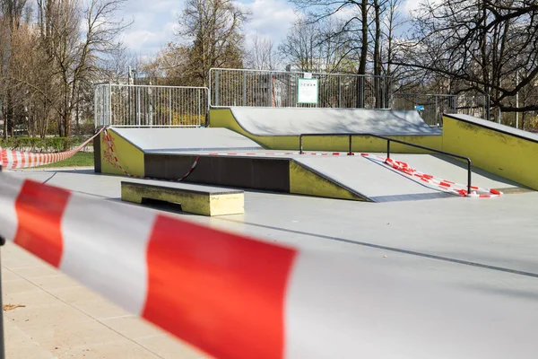 Restrição do vírus Corona COVID-19. Não há pessoas devido à quarentena. Parque de skate urbano fechado. Parque vazio e parque infantil. Fique em casa compaign. Fita de aviso vermelha em rampas e escorregas. Distanciamento social — Fotografia de Stock