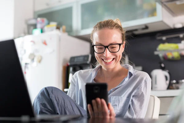 Restez à la maison et à distance sociale. Femme dans ses vêtements de maison occasionnels travaillant à distance de la table à manger de la cuisine. Chat vidéo sur les réseaux sociaux avec des amis, des membres de la famille, des entreprises ou des partenaires — Photo