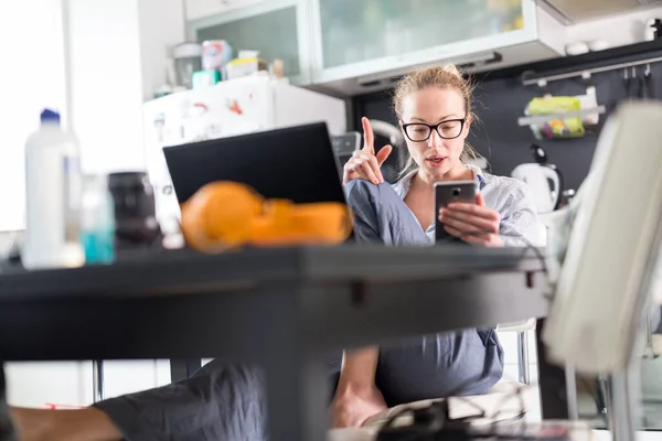 Maradj otthon, és maradj távol a társadalomtól. Egy nő az alkalmi otthoni ruhájában, aki távolról dolgozik a konyhaasztaltól. Videochat a közösségi média segítségével barátokkal, családtagokkal, üzleti ügyfelekkel vagy partnerekkel — Stock Fotó