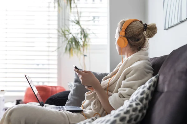 Distanciamiento social. Quédate en casa. Mujer en albornoz siendo cómoda en su sofá en casa, utilizando aplicaciones de redes sociales en el teléfono para el chat de vídeo y atascado conectado con sus seres queridos . — Foto de Stock