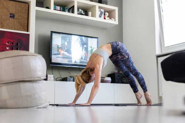 Atrakcyjna sportowa kobieta ćwicząca w domu, ćwicząca pilates przed telewizorem w swoim salonie. Oddalenie się od społeczeństwa. Bądź zdrowy i pozostań w domu podczas pandemii wirusa korony — Zdjęcie stockowe