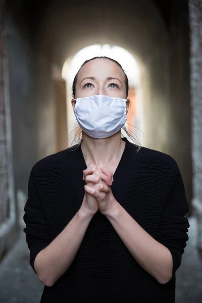 Surto de coronavírus. Mulher caucasiana jovem vestindo máscara facial proteção médica orando sobre coronavírus pandemia global, para a salvação da humanidade, saúde, ansiedade e redução da depressão — Fotografia de Stock