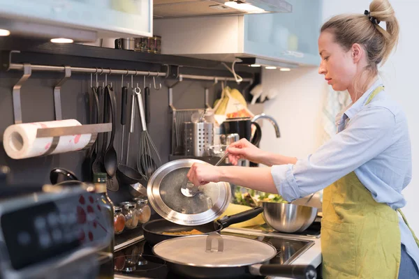 Rester à la maison femme au foyer cuisine dans la cuisine, mélanger le plat de friture dans une casserole, préparer la nourriture pour le dîner de famille . — Photo