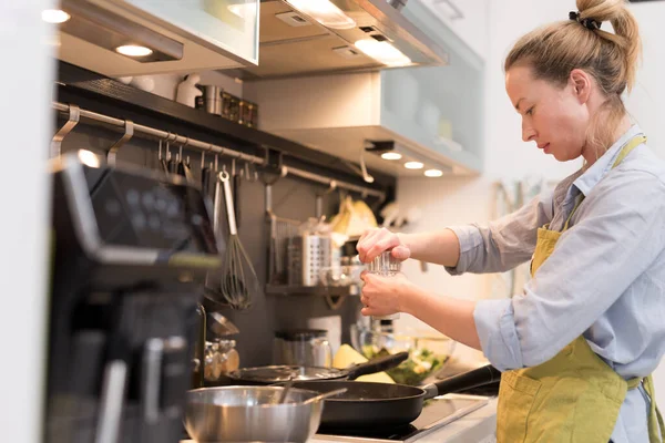 Rester à la maison femme au foyer cuisine dans la cuisine, saler le plat dans une casserole, préparer la nourriture pour le dîner de famille . — Photo