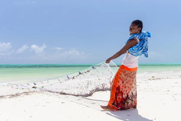 Традиционная африканская местная сельская рыбалка на пляже Падже, Занзибар, Танзания. Традиционно одетая местная женщина тянет рыболовные сети, ловит мелкую рыбу . — стоковое фото