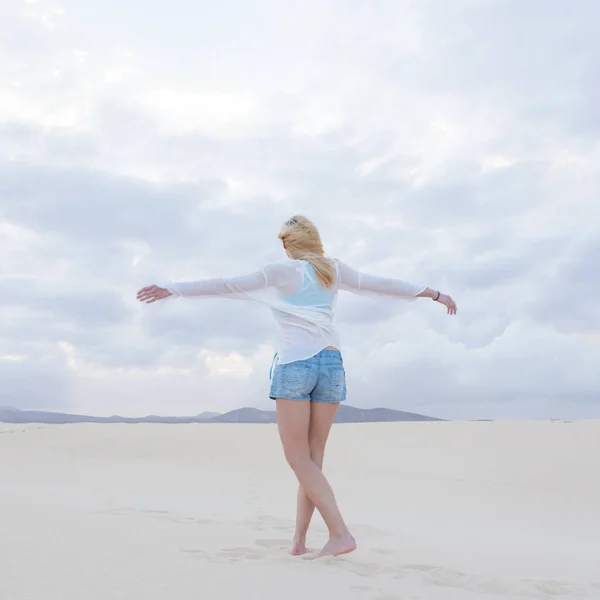 Беззаботная женщина наслаждается свободой на белом песке дюны в сумерках . — стоковое фото