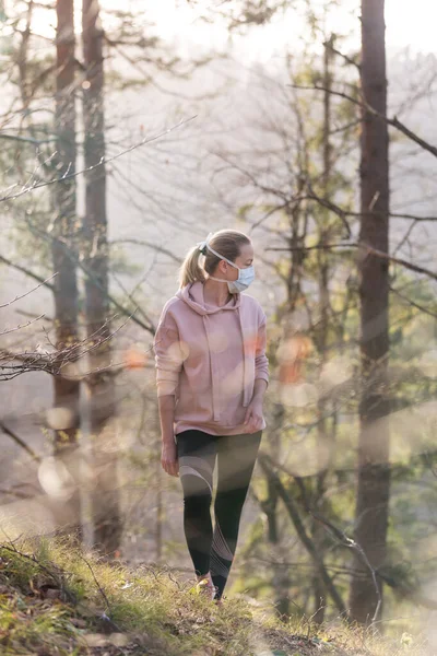 Corona virus, or Covid-19, is spreading all over the world. Portrait of caucasian sporty woman wearing a medical protection face mask while walking in the forest. Corona virus. — Stock Photo, Image