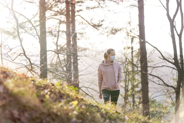 Das Coronavirus oder Covid-19 breitet sich auf der ganzen Welt aus. Porträt einer kaukasischen sportlichen Frau, die beim Spazierengehen im Wald eine medizinische Schutzmaske trägt. Coronavirus. — Stockfoto