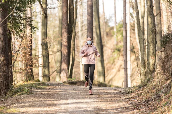 Corona virus, nebo Covid-19, se šíří po celém světě. Portrét kavkazské sportovní ženy v ochranné masky obličeje při běhu v přírodě. — Stock fotografie