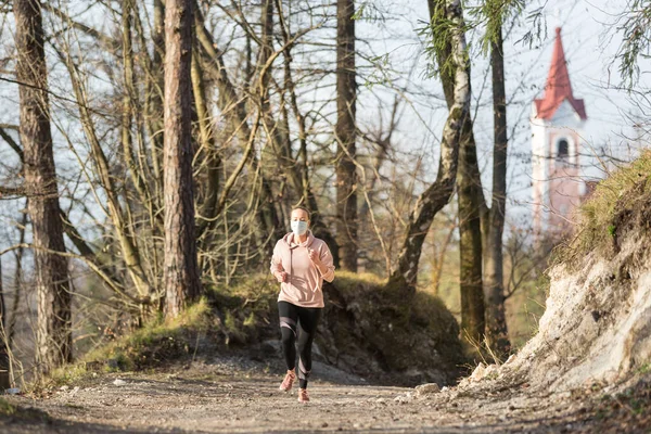 A Corona vírus, vagy Covid-19, elterjedt az egész világon. Portré fehér sportos nő visel orvosi védelem arc maszk futás közben a természetben. — Stock Fotó