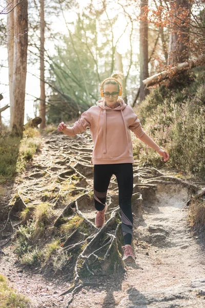 Active sporty woman running in autumn fall forest jumping over the roots on the path. Healthy lifestyle image of young active caucasian woman jogging outside in nature — Stock Photo, Image