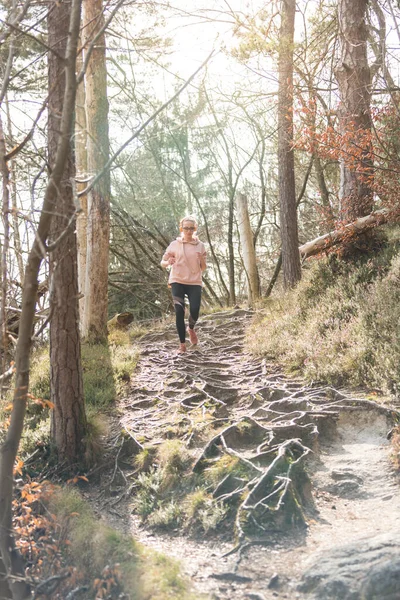 Actieve sportieve vrouw die naar de muziek luistert terwijl ze in het herfstbos rent. Vrouwelijke loper training buiten. Gezond levensstijl imago van jonge blanke vrouw joggen buiten — Stockfoto