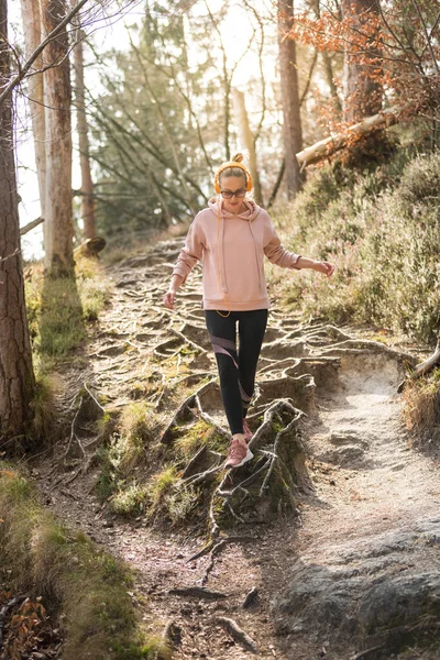Mujer deportiva activa corriendo en otoño bosque de otoño saltando sobre las raíces en el camino. Estilo de vida saludable imagen de la joven mujer caucásica activa corriendo fuera en la naturaleza —  Fotos de Stock
