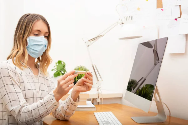 Young business woman measuring fever and wearing protective mask, working from home