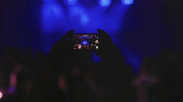 Real live streaming in disco hall during party. Silhouette hands of audience taking photo with mobile phone. Recording Video in party.