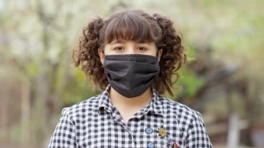 Coronavirus salgını sırasında kameraya bakan maske takan küçük bir kız. COVID-19 karantina virüsü sırasında. Kırmızı kamera yavaş çekim görüntüsü. Maskeli kız.
