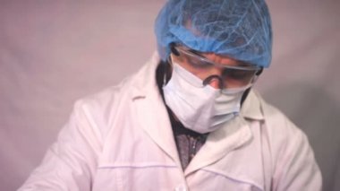 Yorgun Doktor, koronavirüs testinin sonucuna bakıyor ve masada uyuyor. Profesyonel önlük giyiyor. Doktor iş yerinde uyur ve sağlık tulumu giyer..