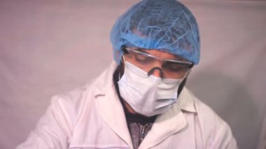 Yorgun Doktor, koronavirüs testinin sonucuna bakıyor ve masada uyuyor. Profesyonel önlük giyiyor. Doktor iş yerinde uyur ve sağlık tulumu giyer..