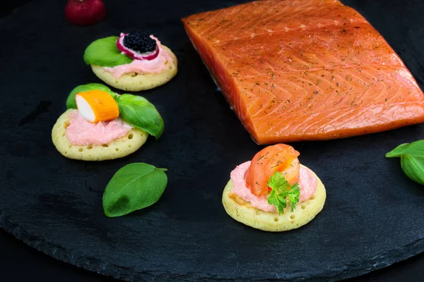 Canapés de panqueca caseiro e pedaço de salmão defumado em placa de pedra de ardósia para festa de comida de dedo — Fotografia de Stock