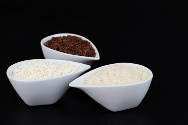 3 çeşit çiğ Tay Tay Jasmine rice(Hom Mali), Glutinous/yapışkan pirinç (Khao VINN), kahverengi pirinç (Khao Dum) kopya alanı siyah zemin üzerine beyaz bardak pirinç