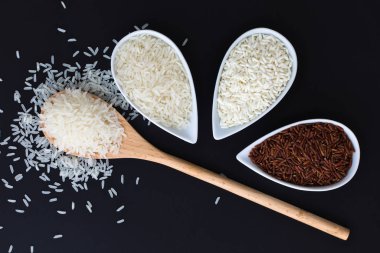 3 çeşit çiğ Tay Tay Jasmine rice(Hom Mali), Glutinous/yapışkan pirinç (Khao VINN), kahverengi pirinç (Khao Dum) kopya alanı siyah zemin üzerine beyaz bardak pirinç