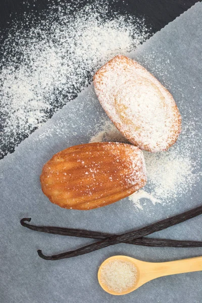 Fresh bake mini cake madeleines icing sugar on top with vanilla bean and teaspoon of sugar on black slate plate — Stock Photo, Image