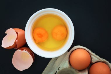 organic eggs and yolk broken in white cup on black background clipart