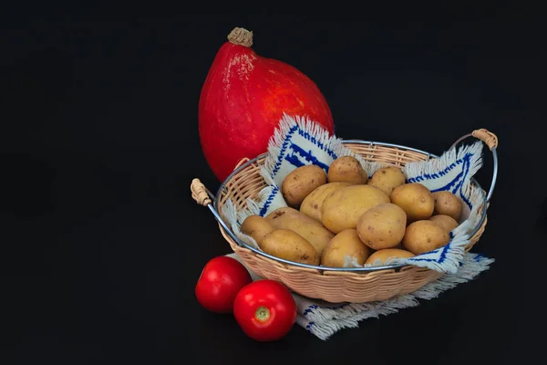 Organic potatoes in the basket, tomatoes and pumpkin on black back ground — Stock Photo, Image