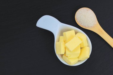 Beyaz fincan tereyağı ve kopya alanı ile siyah arduvaz plaka üzerinde tahta kaşık şeker