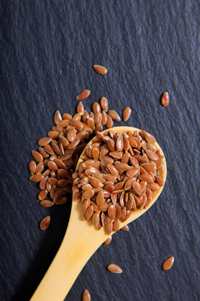 Tahta kaşık siyah arduvaz taş plaka üzerinde organik keten tohumu kapatın 