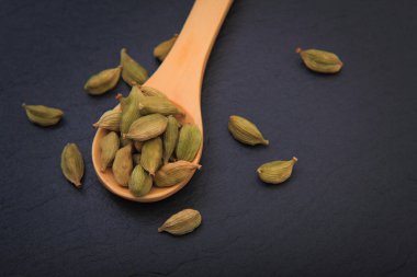 Metin için kopya siyah arduvaz zemin üzerine tahta kaşık içinde Cardamoms sağlıklı gıda kavramı Aroma baharat kurutulmuş