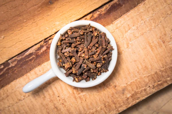 Concept d'épices exotiques clous de girofle bio en tasse blanche sur fond bois — Photo