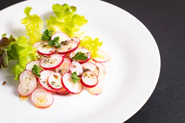 Healthy food organic slices radish salad in white plate on black