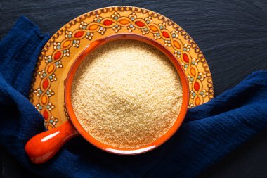 Gıda konsepti, portakal kâsesinde organik ham kuskus Blask taş tahtada fotokopi alanı ile.