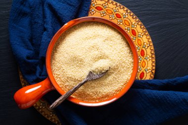 Gıda konsepti, portakal kâsesinde organik ham kuskus Blask taş tahtada fotokopi alanı ile.
