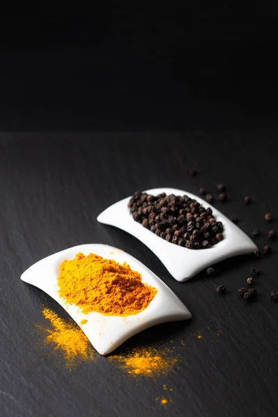 Healthy food and alternative medicine ingredient concept organic turmeric powder  Black peppers and  in square ceramic cup on black slate stone board with copy spac