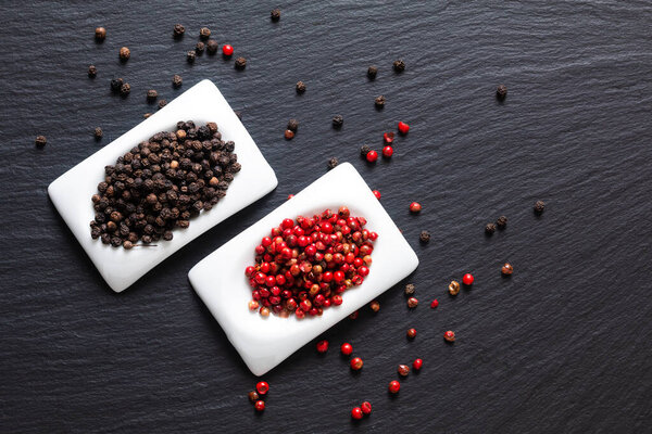 Healthy food ingredient concept organic Black peppers and red peppercorns in square ceramic cup on black slate stone board with copy spac