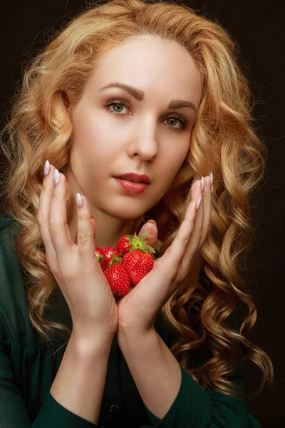 Beautiful resilient young girl holding a strawberry. Portrait in the studio background