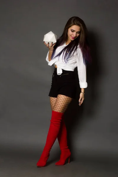 Girl brunette in a white shirt and red boots and stockings in a large mesh on a gray studio background in full height.